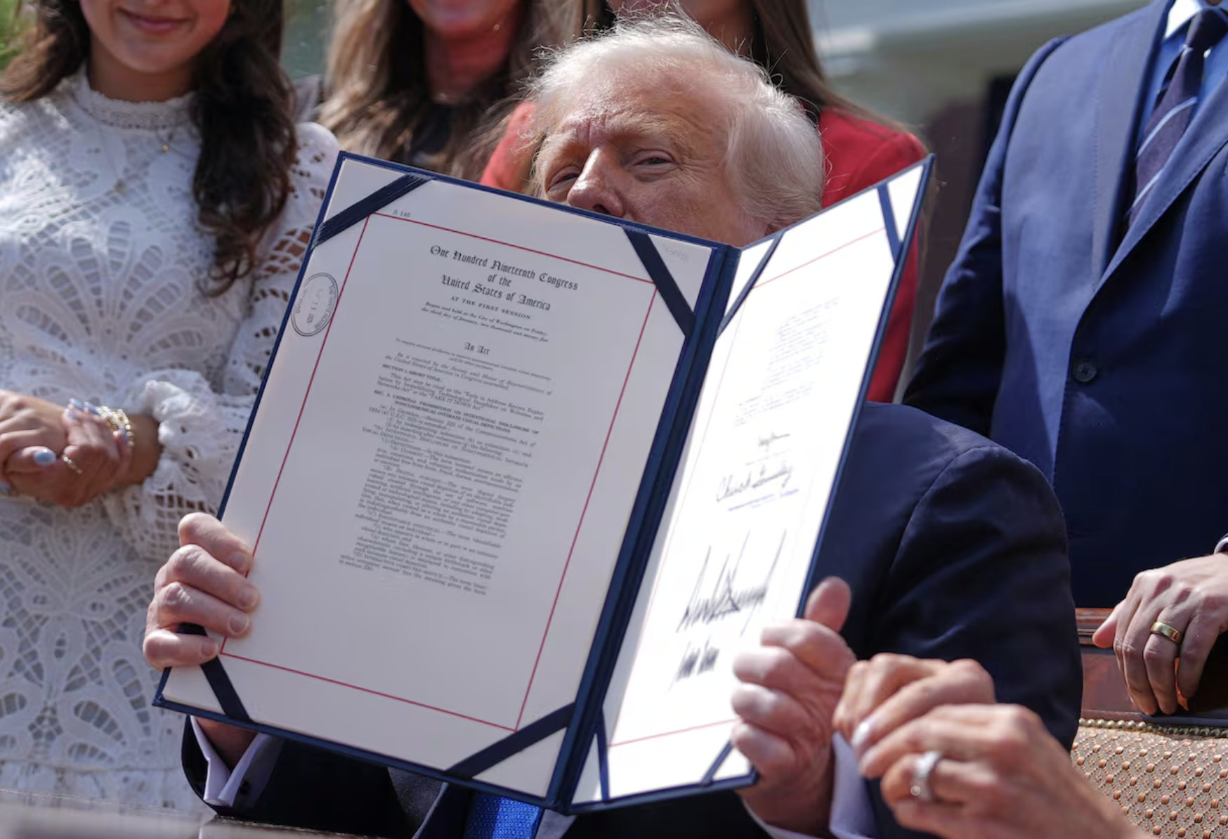 President Donald Trump holds up the signed TAKE IT DOWN Act at the May 2025 bill-signing ceremony, the federal law whose first convictions and prosecutions in April and May 2026 are covered in this post; First Lady Melania Trump, who championed the legislation, is visible at left.
